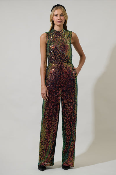 model wearing an iridescent sequin jumpsuit with shades of green, yellow, orange, and purple. Jumpsuit is sleeveless, has a mock neck, asymmetrical draped bodice detail and wide leg pants. Shown from front