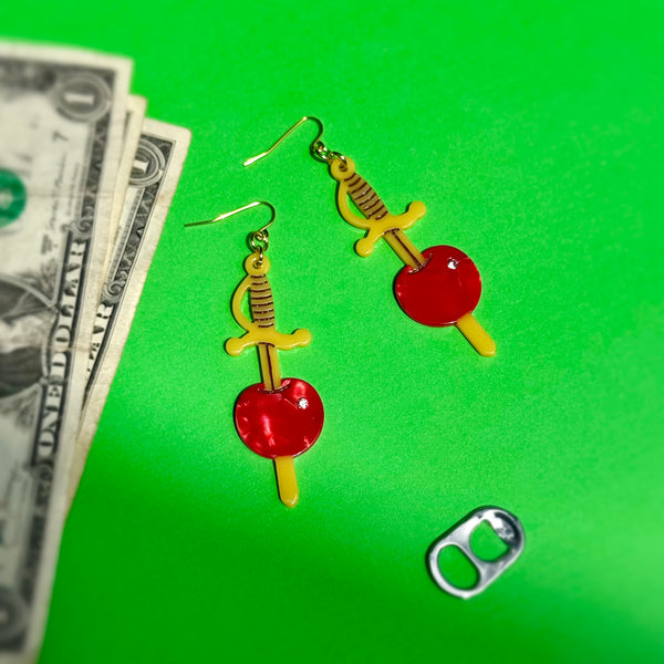 acetate dangle earrings in the shape of a pair of yellow cocktail sword skewers with a marbled maraschino cherry with silver rhinestone decoration. Shown flat