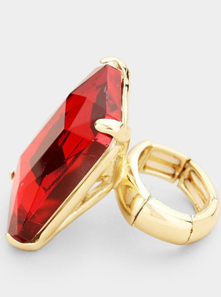  rectangular faceted red plastic jewel set on a gold metal ring with an adjustable segmented stretch band, shown from the side