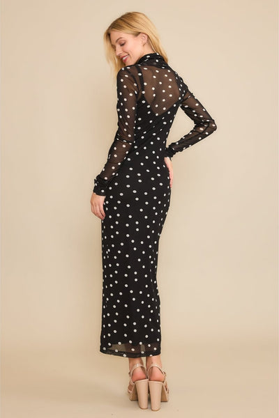Model wearing a black and white polka dot mesh midi length dress with long sleeves. It has a matching black v-neck spaghetti strap slip underneath. Shown from the back