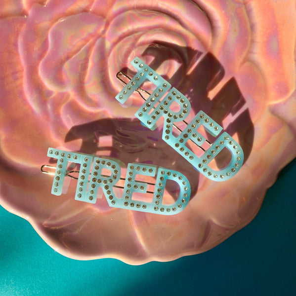pair of acetate baby blue barrettes spelling the word TIRED with silver rhinestone embellishments. Shown flat