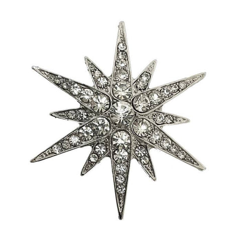 Starburst -shaped silver metal brooch with crystal-like stones on a white background