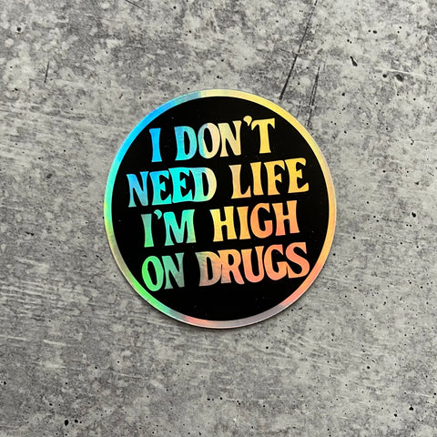 round holographic vinyl sticker with black negative space lettering and message “I Don't Need Life I'm High On Drugs” 