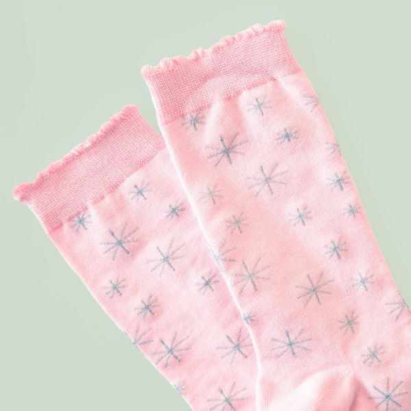 light pink unisex cotton crew socks with silver lurex star patterns shown in close up on a blue background