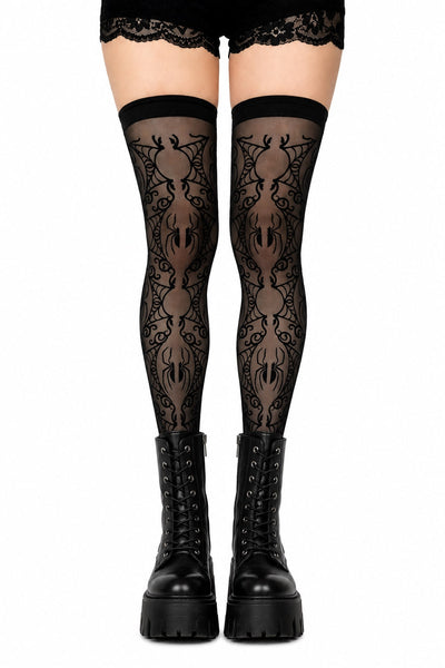 model wearing sheer black stay up thigh highs with allover flocked pattern of spiders and filigree webs. Shown from front