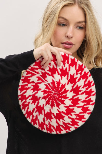 Woman holding a red and white houndstooth patterned knit beret against a plain background