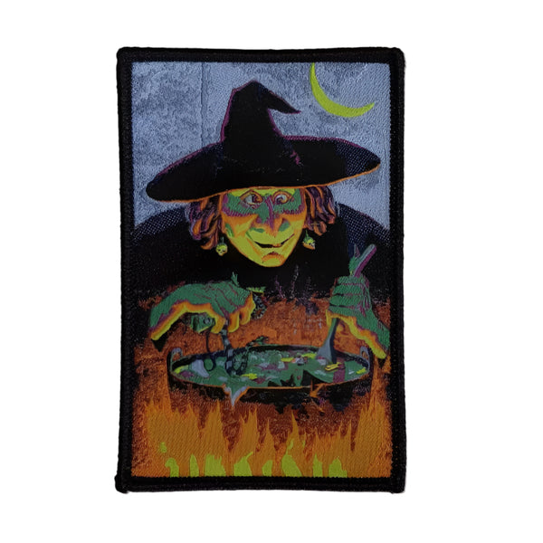 Rectangular woven patch with black embroidered border and image of a witch standing below a crescent moon above a large cauldron 