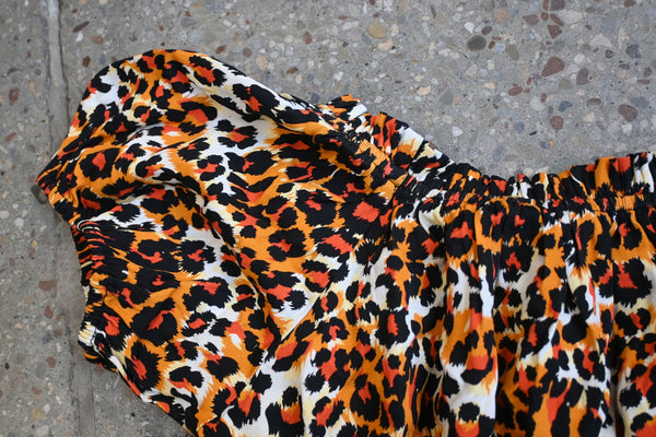 Orange, white, and black leopard print patterned rayon crop peasant blouse style top with wide rounded neckline, cap sleeves, and elasticized hemming at neckline, sleeves, and bottom hem. Shown from front lying flat In close up of sleeve