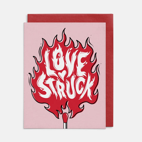 Greeting card with 'Love Struck' design in flames with match head on a pink background. Shown from front with matching red envelope 