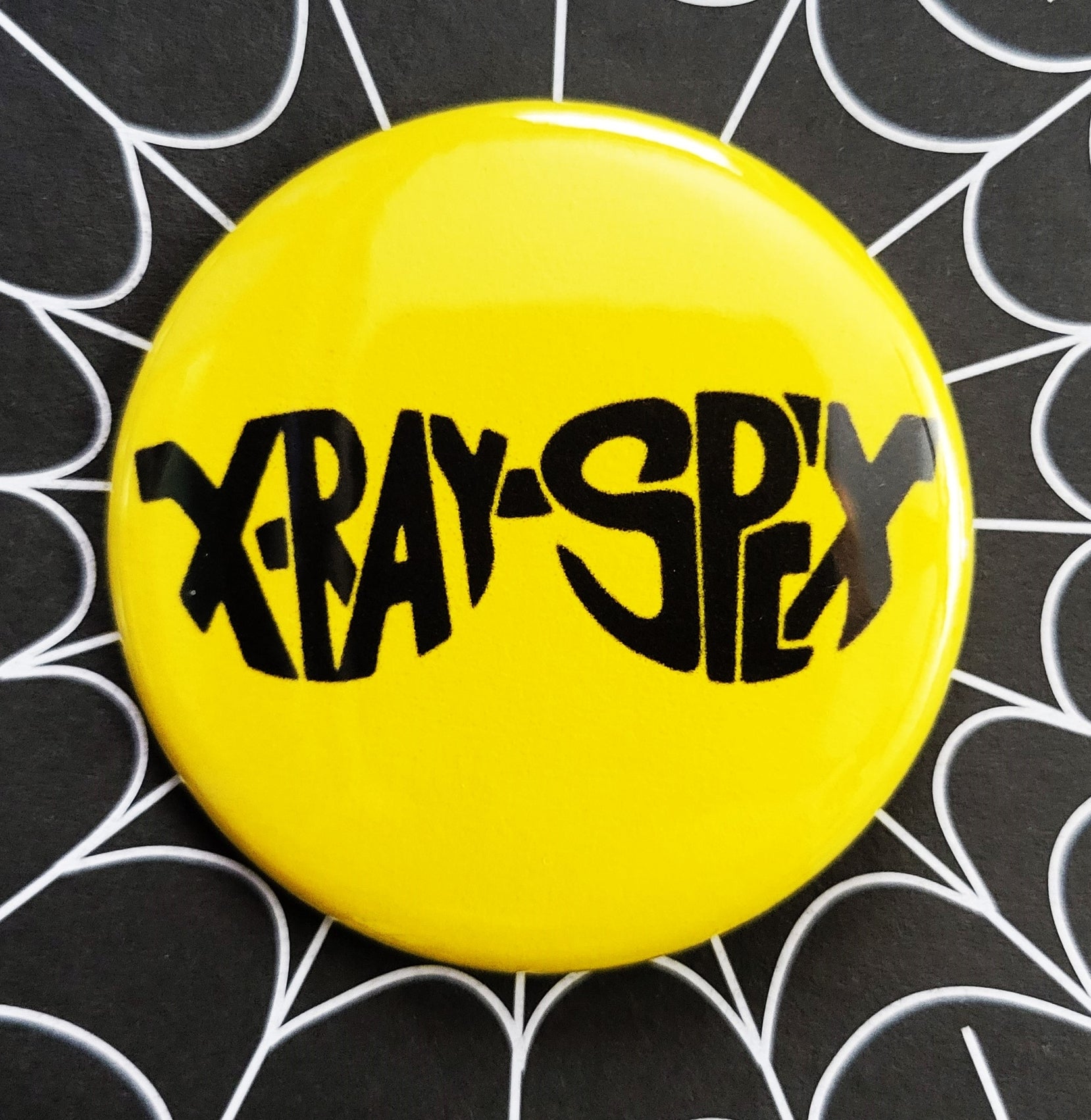 1.25” pinback button of X-Ray Spex glasses shaped band logo on a bright yellow background 