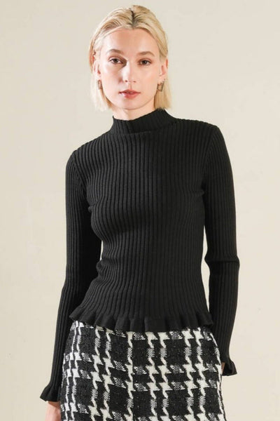 model wearing ribbed knit black mock turtleneck with long sleeves and ruffle detail at each cuff and bottom hem. Shown from the front