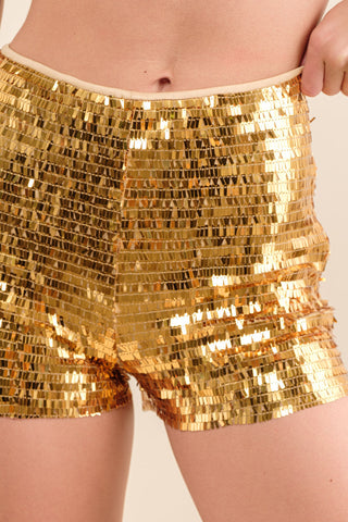 Gold sequin short shorts worn by a person on a plain background. Shown up close from the front