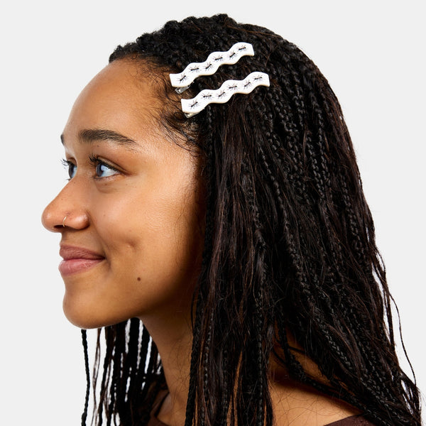 set of two bright white acetate alligator style hair clips in a wavy rectangle shape with painted detail of rows of ants along each clip. Shown in model's hair