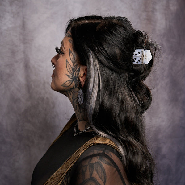 Model wearing marbled white acetate claw style hair clip in the shape of a die with black pips in hair up half down hairdo