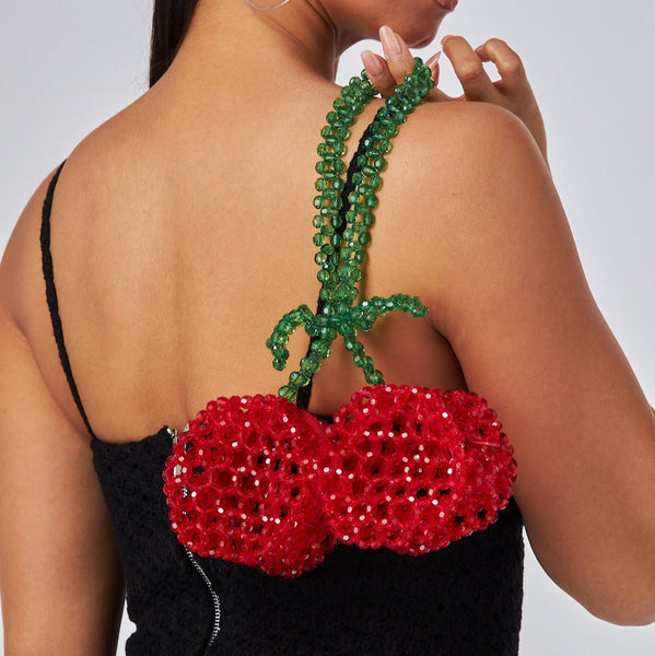 Plastic shiny faceted bead purse in the shape of red pair of cherries with green leaves and stem handle. Shown held over model’s shoulder