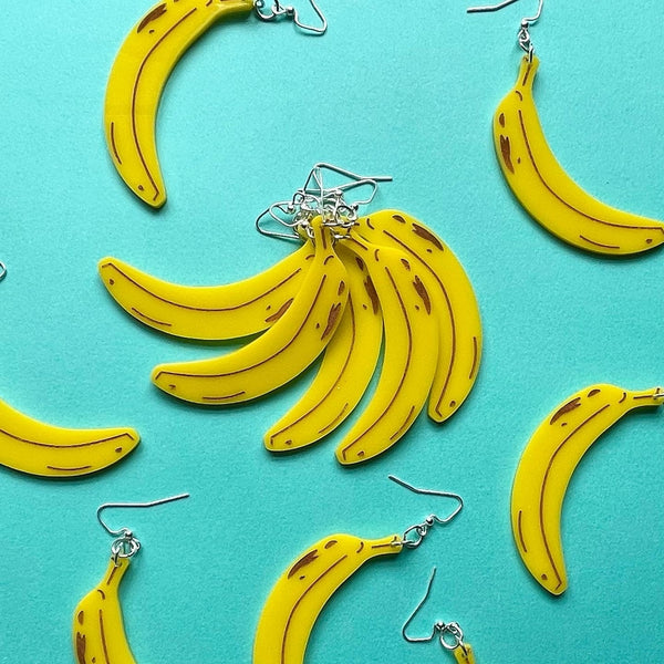 yellow banana shaped laser cut acrylic earrings with etched brown "ripeness" details, with several shown gathered together as a bunch
