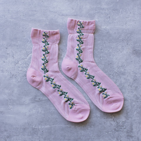 Light pink cotton socks with a knit-in pattern of purple, white, and green flowers and panels of patterned mesh. Shown flat