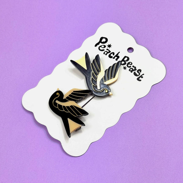 pair of black and gold acetate sparrow shaped barrettes with gold jewel eyes. Shown on backing card on purple background