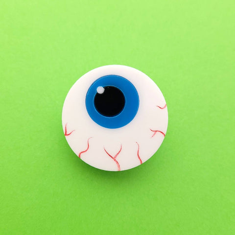 Round layered laser-cut acrylic brooch of a cartoony bloodshot eyeball with a bright blue iris. Shown flat from the front