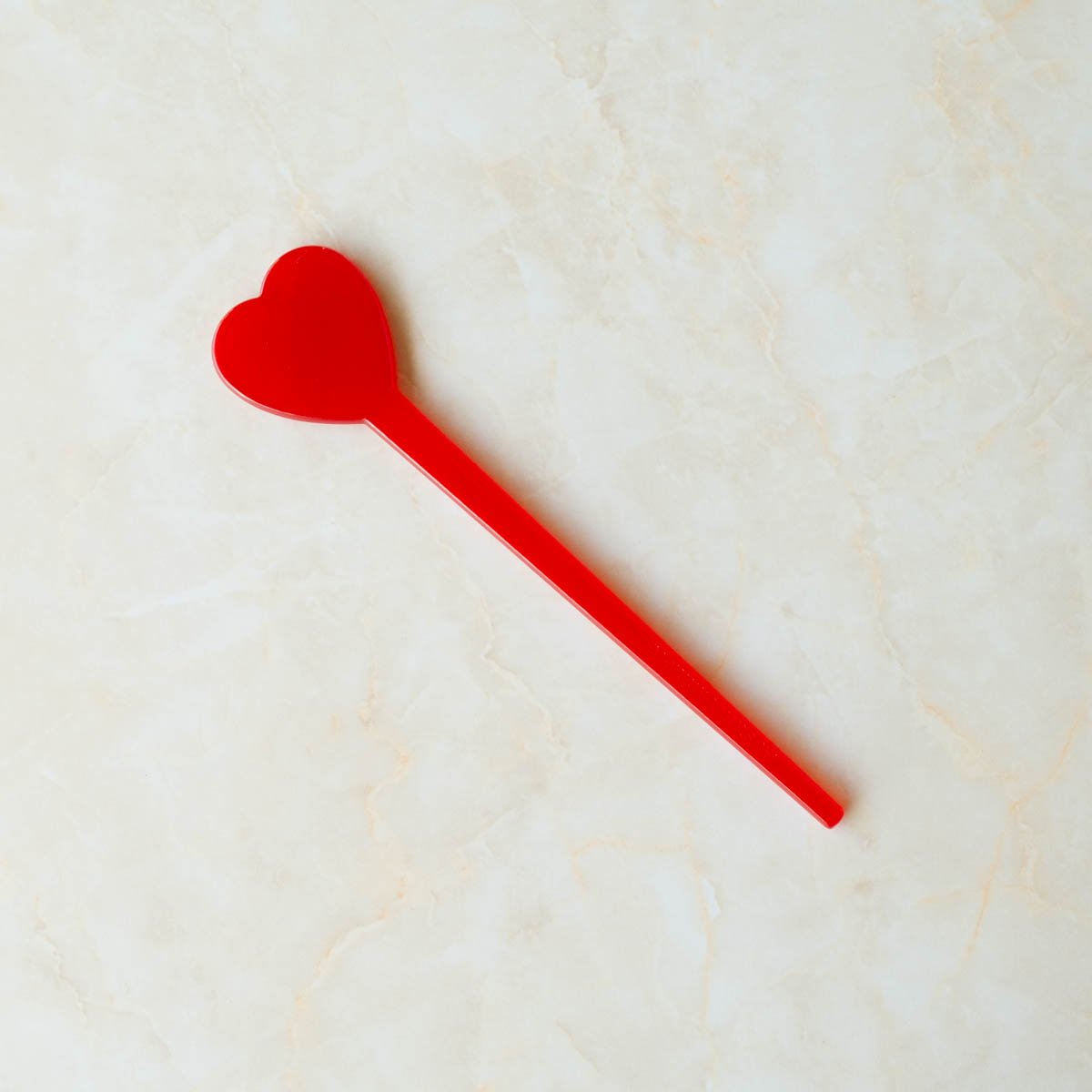 Acetate hair stick with a heart shaped topper in a shade of bright red. Shown flat.