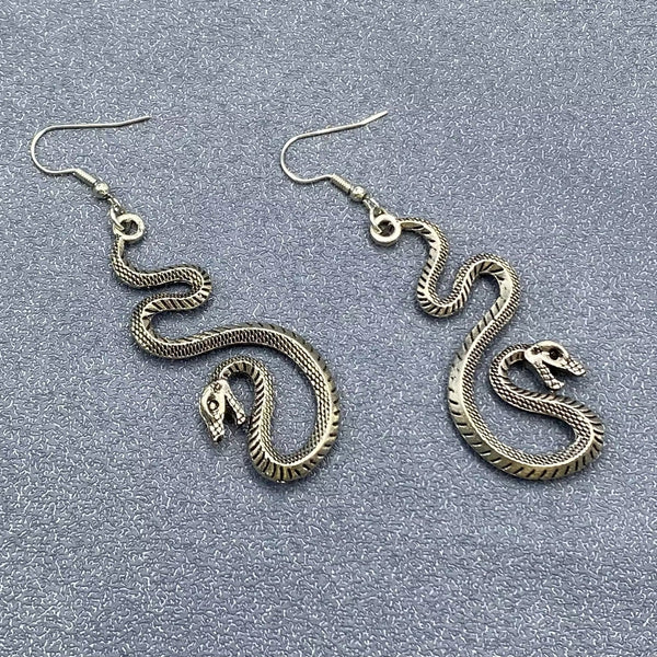 Pair of burnished silver metal hissing detailed snake dangle earrings. Shown flat to display detail on both sides of charms