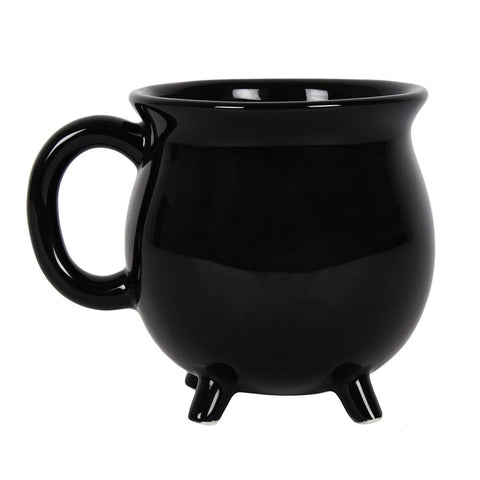 Black shiny glazed ceramic mug in the shape of a cauldron with four small feet at the bottom. Shown from the front