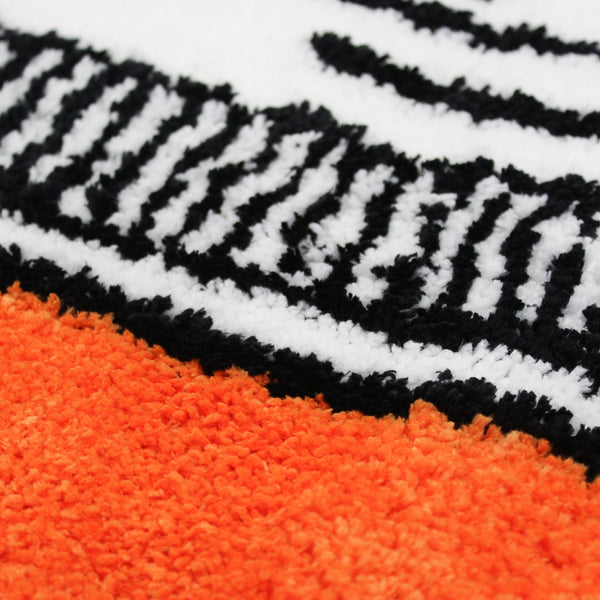 A tufted rug shaped like an orange prescription pill bottle with a white label, black border, and blue Rx symbol, shown from the front on a plain white background. Detail shot of colors