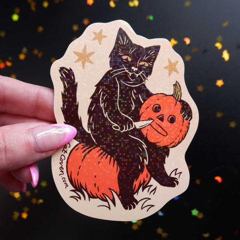 die cut sparkly vinyl sticker of a black cat sitting on a pumpkin carving a jack-o'-lantern