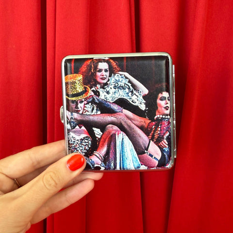 Cigarette case with faux leather textured exterior and printed image of Magenta, Columbia, and Dr. Frank N. Furter from the Rocky Horror Picture Show. Shown held in front of red background