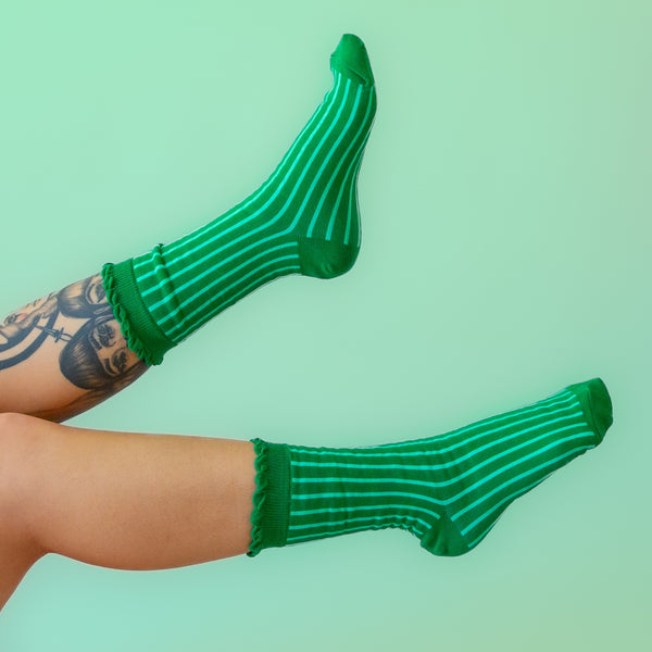kelly green cotton socks with mint green stripes and ruffled green cuffs shown worn by a model on light green background