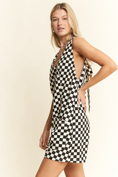 model wearing a black and white checker print cotton blend relaxed fit romper with wide straps, slightly rounded v-neckline, self-tie detail at back, relaxed fit shorts with patch pockets. Shown from side