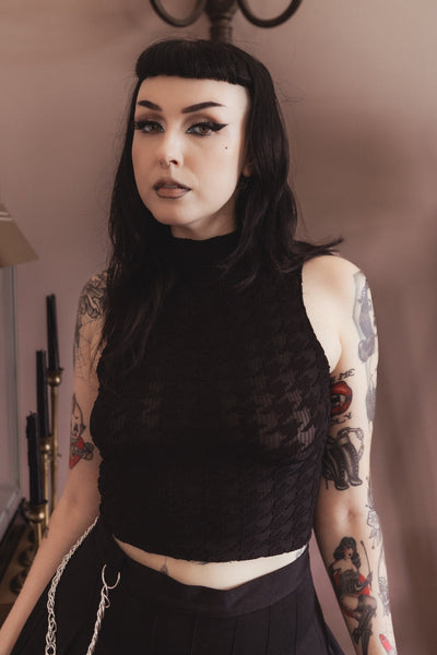 model wearing a black sheer mock neck sleeveless crop top with a ribbed base pattern and all over large houndstooth print. Shown from front