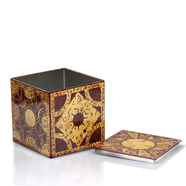 A decorative square tin box with an intricate gold and dark brown geometric and calligraphic pattern made to resemble the Lament Configuration puzzle box from Hellraiser, shown on a reflective white surface against a white background. Shown with lid off