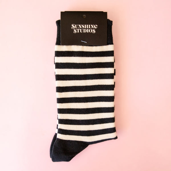 Pair of off-white crew socks with black ruffle cuff, black and white horizontal stripe, and black toes and heels; Shown in card packaging