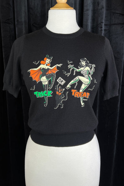 black crew neck short sleeved sweater with retro women wearing bat costume and mummy costume alongside a black cat with message "TRICK OR TREAT". Shown on dress form