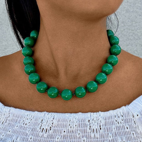 Green beaded necklace worn by a person with a white top against a neutral background