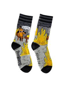 black, grey, yellow, and orange unisex crew socks with black and grey stripe cuffs and black toes/heels with all over pattern of a cartoon dog wearing a hat sitting at a kitchen table surrounded by flames with a speech bubble saying "THIS IS FINE." Shown flat