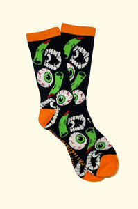 black cotton crew socks with orange cuffs, heels, and toes with an all-over pattern of plastic vampire teeth, witch fingers, and green bloodshot eyeballs. Shown flat