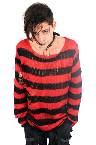 Model wearing an open knit oversized sweater with black and red stripes and distressed detail at the sleeve and body. Shown from the front