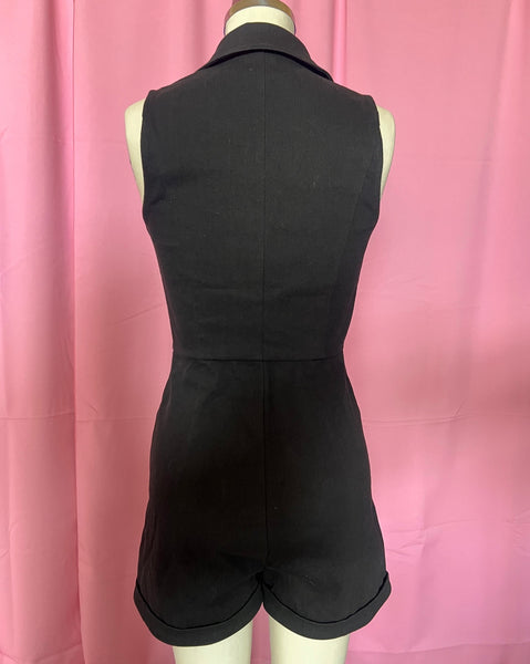 Black cotton blend stretch denim sleeveless romper with pointed collar, silver zipper running down the length of the piece, vertical seaming, red embroidered diagonal heart and arrow detail at the front yoke, red embroidered arrow detail below the diagonal pockets, and cuffed slightly flared shorts. Shown from the back on dress form