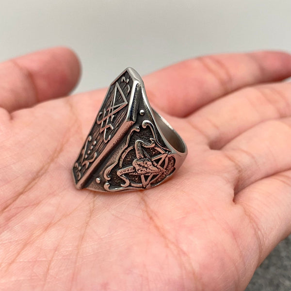 A stainless steel ring with dark antiqued detailing in the shape of a coffin decorated with various occult symbols. Shown from the side 