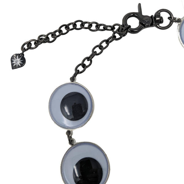 Choker style necklace with 8 linked large plastic black and white googly eyes with gunmetal finish metal link chain extender and matching swivel hook clasp closure. Shown flat in close up of swivel hook