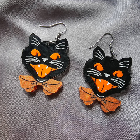Laser-cut layered acrylic dangle earrings in the shape of vintage inspired Halloween marbled black cat heads with orange eyes and open mouths & orange marbled bow ties