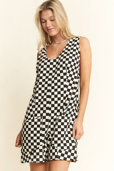 model wearing a black and white checker print cotton blend relaxed fit romper with wide straps, slightly rounded v-neckline, self-tie detail at back, relaxed fit shorts with patch pockets. Shown from front in close up