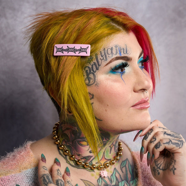 model wearing baby pink rectangular acetate barrette with French style closure and carved black detail of three links of barbed wire. 