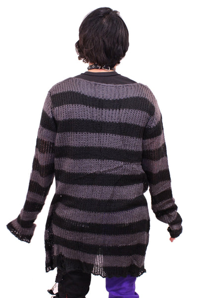 Model wearing an open knit oversized sweater with black and grey stripes and distressed detail at the sleeve and body. Shown from the back