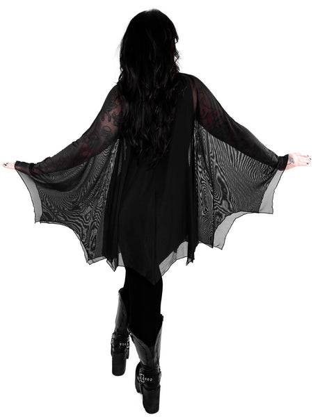 Model wearing a black mesh cape with raw scalloped hemline in the shape of bat wings with sewn in arm holes and a self adjustable front tie. Shown from the back