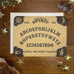 rectangular die cut heavy cardstock letterpress note card designed to resemble a Ouija board, with messages "WITH YOU IN SPIRIT" and "UNTIL WE MEET AGAIN" surrounded by typical layout of a Ouija board in black and brown