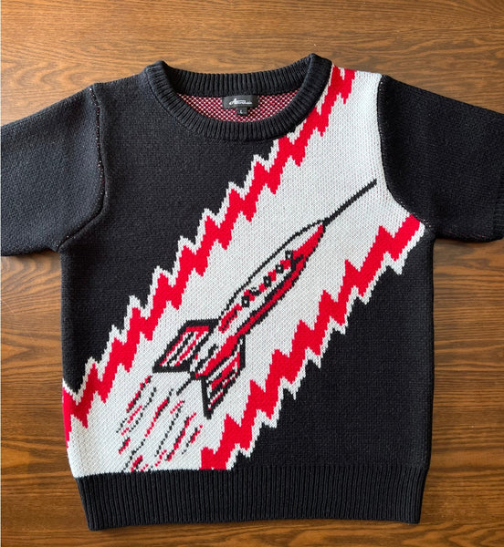 fitted acrylic short sleeve sweater with a retro looking rocket ship on a red, white, and black background. Shown lying flat