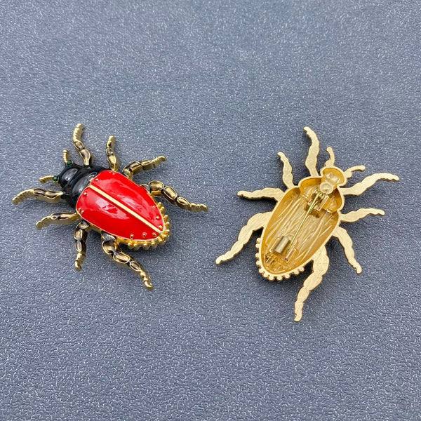 gold metal enameled beetle brooch with bright red enameled abdomen, black head, gold legs, and small green jeweled eyes. Shown flat from front and back